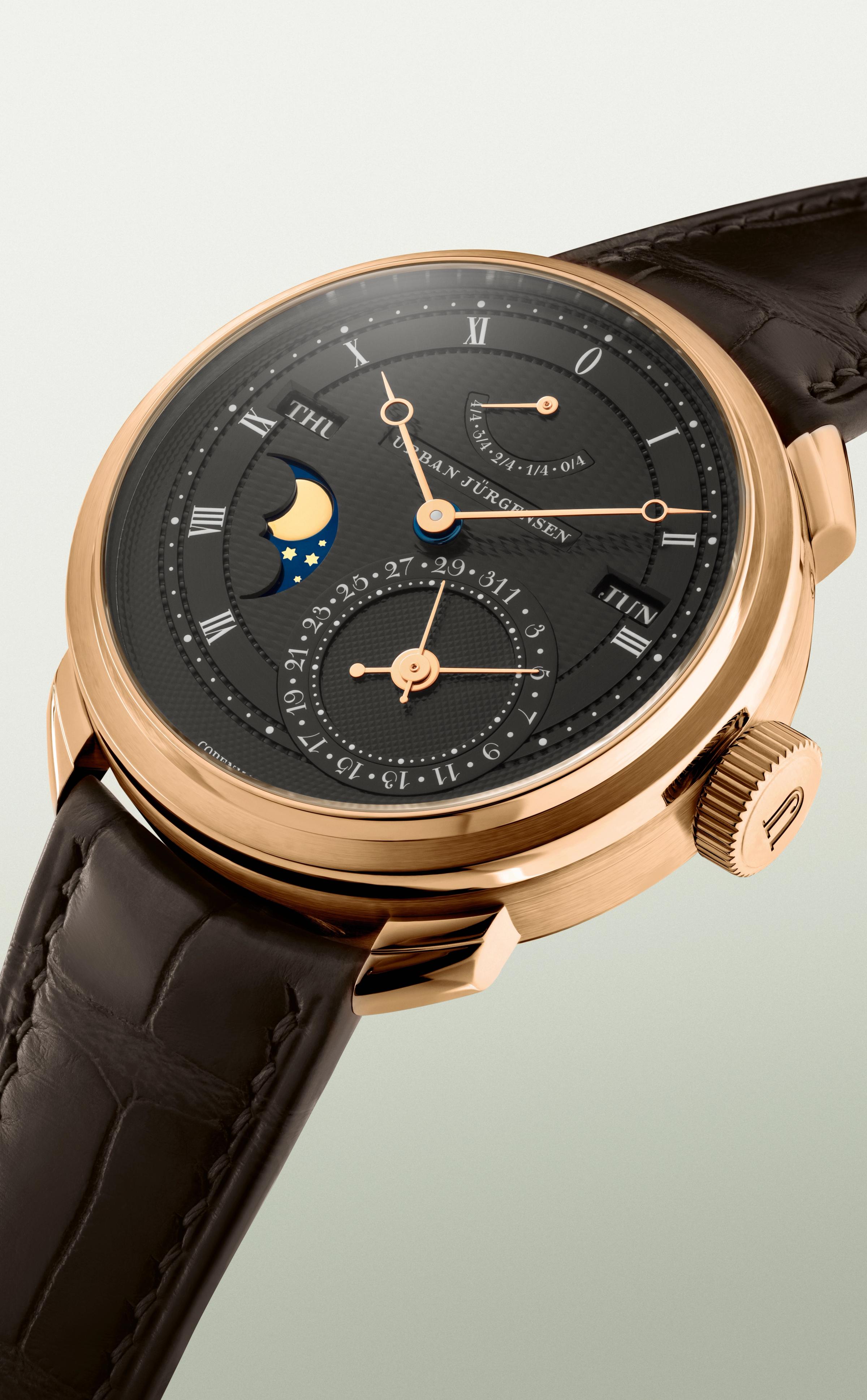 Rose gold Urban Jürgensen wristwatch with dark guilloché dial, moonphase, day and date indicators, power reserve display, and brown leather strap.